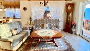 Ein Wohnzimmer mit Sofa, Couchtisch, einer Kandelaber, einer Uhr und Blick durch ein Fenster.