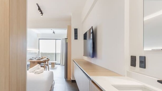 A modern hotel room with a long hallway, a bed, a dining area, and a large mirror. - Myla - 1BR Loft Plus in Condesa with balcony (Mexico City)