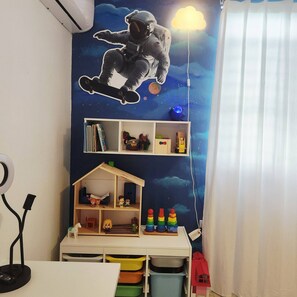 Ein Kinderzimmer mit Wandgestaltung zum Thema Weltraum, einem Holzregal mit Spielzeug und einem kleinen Hausmodell.