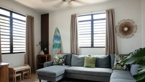 Ein Wohnzimmer mit einem grauen Ecksofa, einem kleinen Holztisch und einer Surfbrett-Dekoration.
