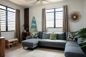 Ein Wohnzimmer mit einem grauen Ecksofa, einem kleinen Holztisch und einer Surfbrett-Dekoration.