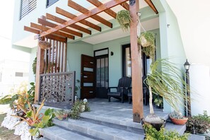 Ein Haus mit einer Holzpergola, einer schwarzen Tür und Topfpflanzen an der Veranda.