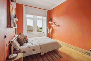 A bedroom with a bed, a window, a wall-mounted shelf, and a rug.