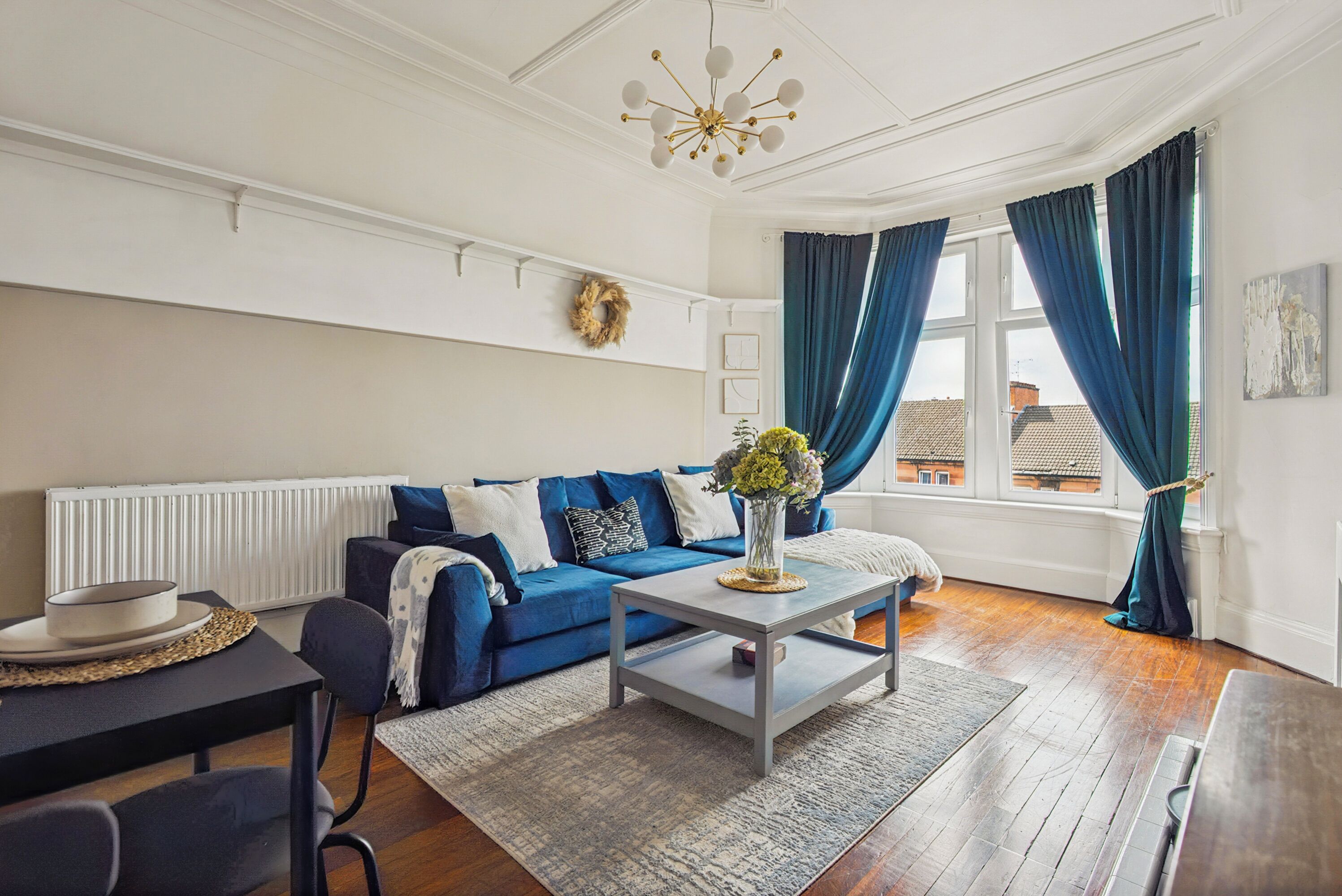 Una sala de estar con un sofá azul, una mesa de centro y un ventanal con cortinas.