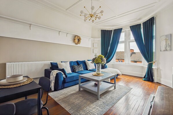 A living room with a blue sofa, a coffee table, and a window with curtains.