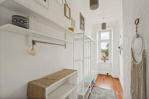 A hallway with white walls, a bench, shelves, and a window with a view.