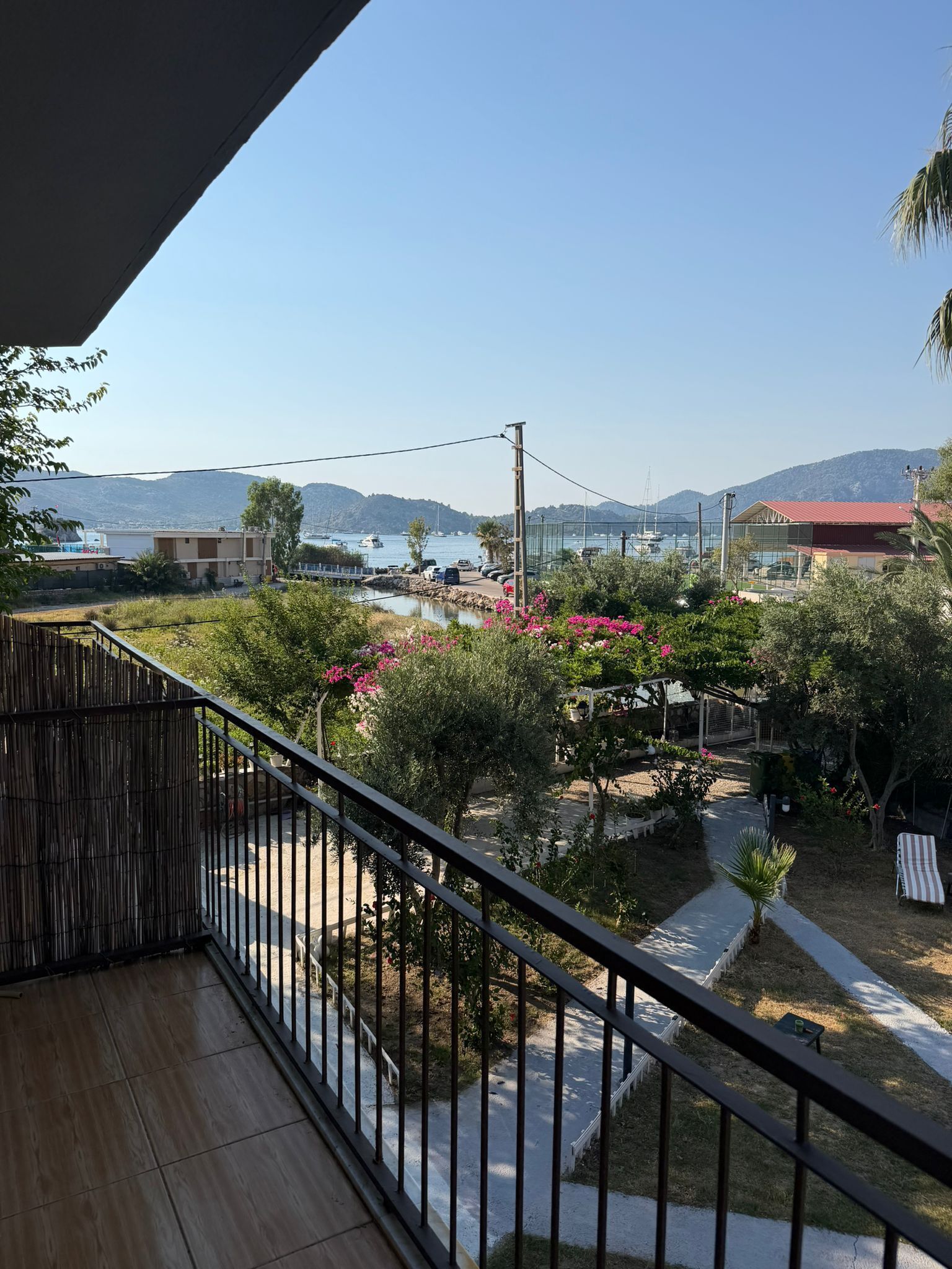Un balcón con vista a un puerto deportivo, barcos y colinas a lo lejos.
