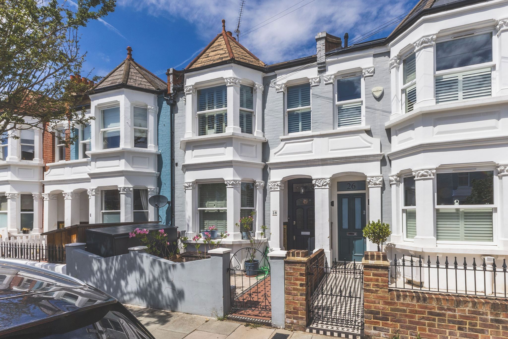 A row of white terraced houses with bay windows, a brick gate, and a car parked in front.