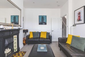 A living room with a fireplace, a black leather sofa, and a coffee table. - Spacious 2BDR 2BA near Shepherds Bush Oasis (Greater London)