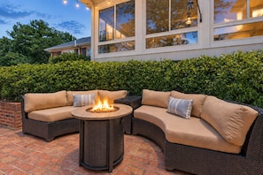 A curved outdoor seating area with a central fire feature, surrounded by a hedge and a building with large windows in the background. - Owens Retreat • Main House + Cottage • Greer, SC (Greer)