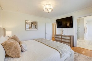 Ein Schlafzimmer mit einem Bett, einer Kommode, einem an der Wand montierten Fernseher und einer Tür zu einem Badezimmer.