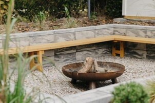 Un jardín con un brasero, bancos de madera y un muro de piedra.
