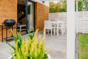 A patio with a barbecue grill, a dining table with chairs, and a white fence. - Chic Holiday Retreat With Sauna in Kopalino (Choczewo)