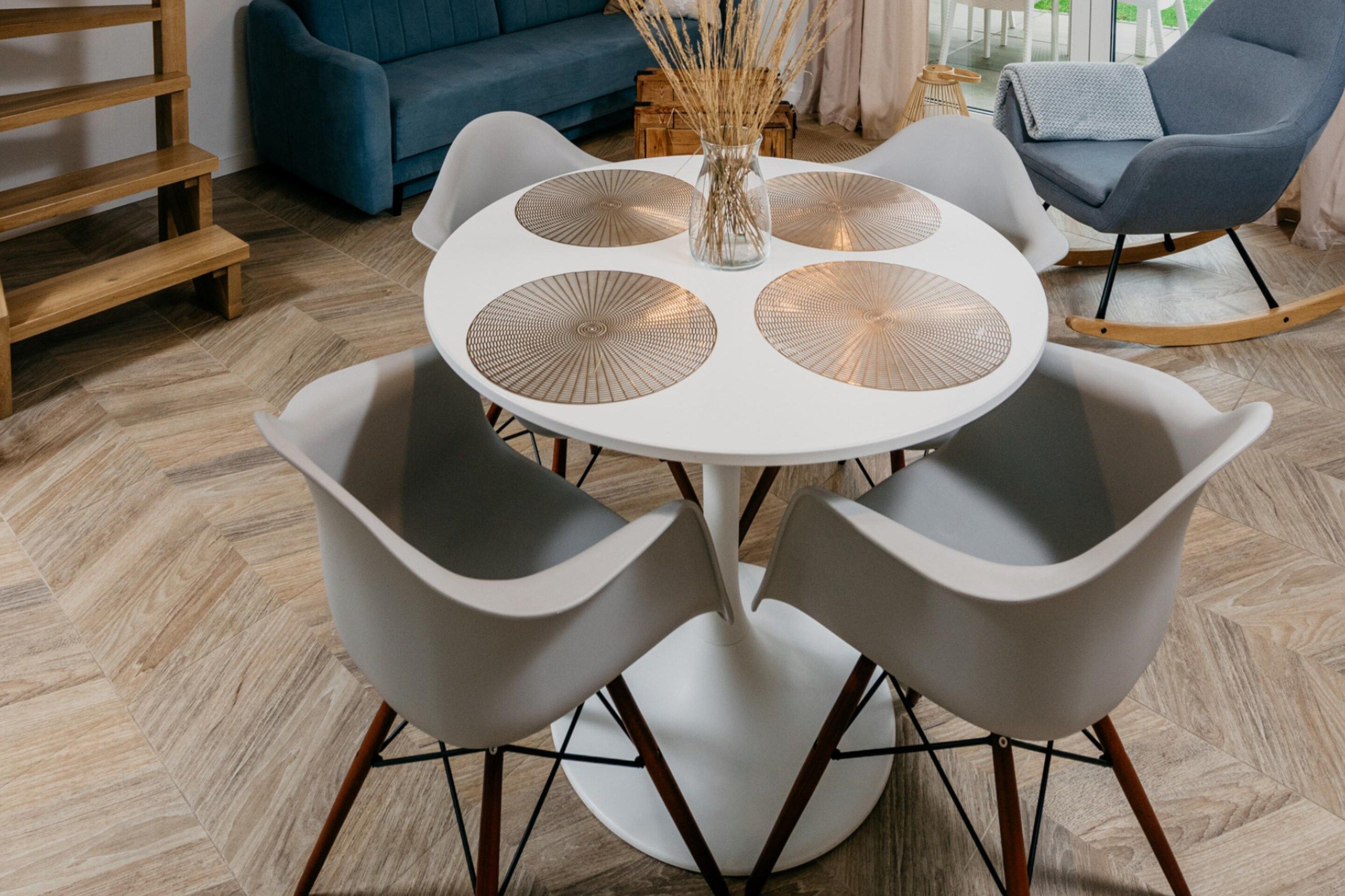 A round table with four grey chairs, a vase with dried plants, and a blue sofa in the background.