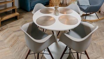A round table with four grey chairs, a vase with dried plants, and a blue sofa in the background.