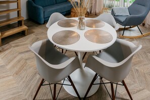 A round table with four grey chairs, a vase with dried plants, and a blue sofa in the background. - Chic Holiday Retreat With Sauna in Kopalino (Choczewo)