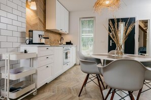 A modern kitchen with white cabinetry, a coffee machine, a built-in oven, and a dining area with a round table and chairs. - Chic Holiday Retreat With Sauna in Kopalino (Choczewo)