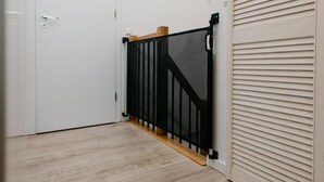 Un couloir avec une porte blanche, une barrière de sécurité noire et un plancher en bois.