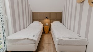 Une petite pièce avec deux lits simples, un tabouret en bois et un luminaire fixé au mur.