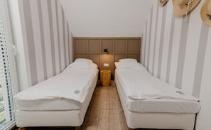 Una habitación pequeña con dos camas individuales, un taburete de madera y una lámpara fijada a la pared.