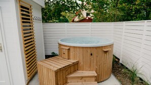 Un bain à remous en bois avec des marches, une clôture blanche et de la verdure en arrière-plan.