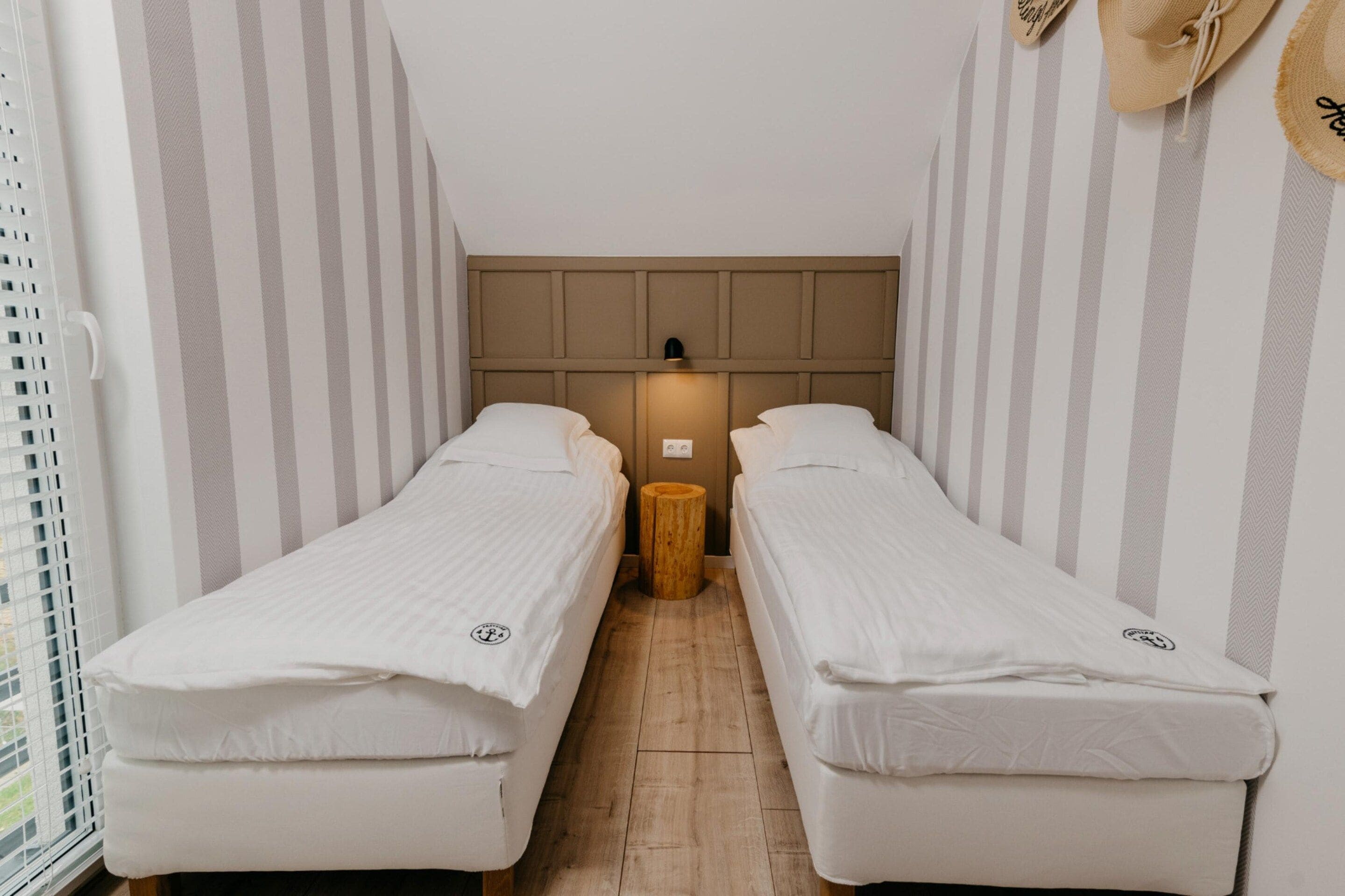 A narrow hotel room with two single beds, a wooden nightstand, and a striped wall pattern.