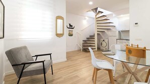 Un interior modern amb una cadira gris, una taula de vidre i una escala espiraltra que porta a una zona de cuina.