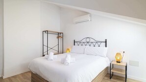 Un dormitori amb un llit, taules de nit, aire condicionat i una prestatgeria penjada.