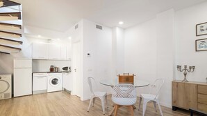 Cuina moderna amb armaris blancs, una rentadora i zona de menjador amb taula de vidre i cadires blanques.