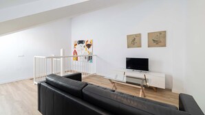 Un saló modern amb un sofà de pell negra, un moble de televisió blanc i obra d'art a la paret.