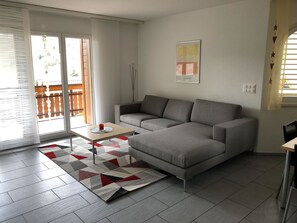 Ein modernes Wohnzimmer mit einem grauen Sofa, einem kleinen Tisch und einem gemusterten Teppich.