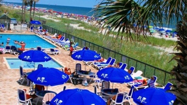 A poolside area with lounge chairs and umbrellas, a pool, and a beach in the background. - Cozy 2-bedroom Oceanfront Family Friendly Condo (Myrtle Beach)