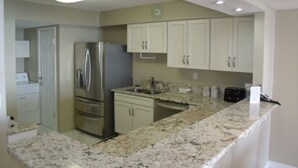 A kitchen with white cabinets, a stainless steel refrigerator, granite countertops, and recessed ceiling lighting. - Cozy 2-bedroom Oceanfront Family Friendly Condo (Myrtle Beach)