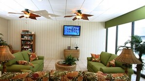 A living room with two green sofas, a television, ceiling fans, and a large window. - Cozy 2-bedroom Oceanfront Family Friendly Condo (Myrtle Beach)