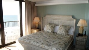 A bedroom with a bed, two bedside tables with lamps, a view of the sea through a sliding door, and a balcony. - Cozy 2-bedroom Oceanfront Family Friendly Condo (Myrtle Beach)
