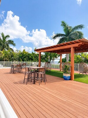 Eine Holzterrasse mit einer Pergola, Sitzmöbeln im Freien und Blick auf das Meer.