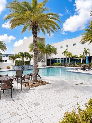 A poolside area with lounge chairs and a palm tree, surrounded by a building with a tiled pool edge. - Waterfront Retreat in Downtown Fort Myers (Fort Myers)