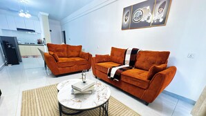 A living room with two orange sofas, a coffee table, and a kitchen in the background. - Modern & Stylish Home (Nairobi)