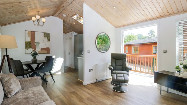 A spacious living area with a wooden ceiling, a dining table with chairs, a sofa, a TV stand, and a view of a wooden cabin through large windows. - Fox Red Retreat (Windermere)