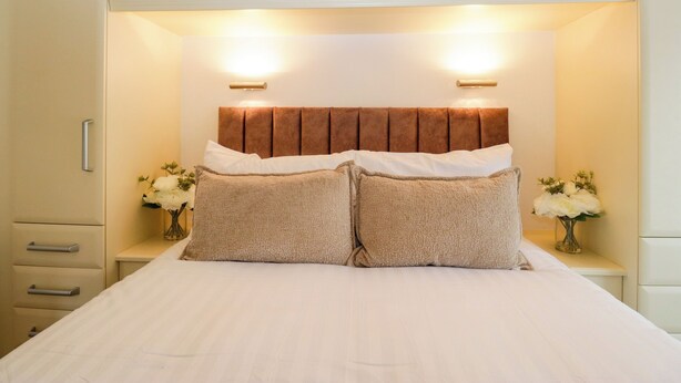 A bed with a headboard, two bedside tables with vases, and a wardrobe above. - Fox Red Retreat (Windermere)