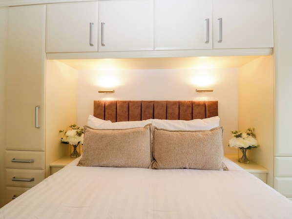 Uma cama com cabeceira, duas mesas de cabeceira com vasos e um guarda-roupa acima.