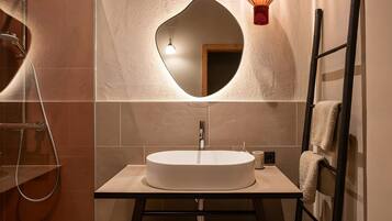 A bathroom with a round sink, a mirror, a towel rack, and a shower.