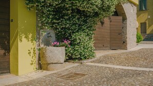 A cobblestone street with a green wall and a stone planter with flowers. - Corte Pulchra - La Lavanda 2 (Pozzolengo)