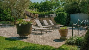 A courtyard with lounge chairs, a large planter, and a staircase leading to an upper level. - Corte Pulchra - La Lavanda 2 (Pozzolengo)