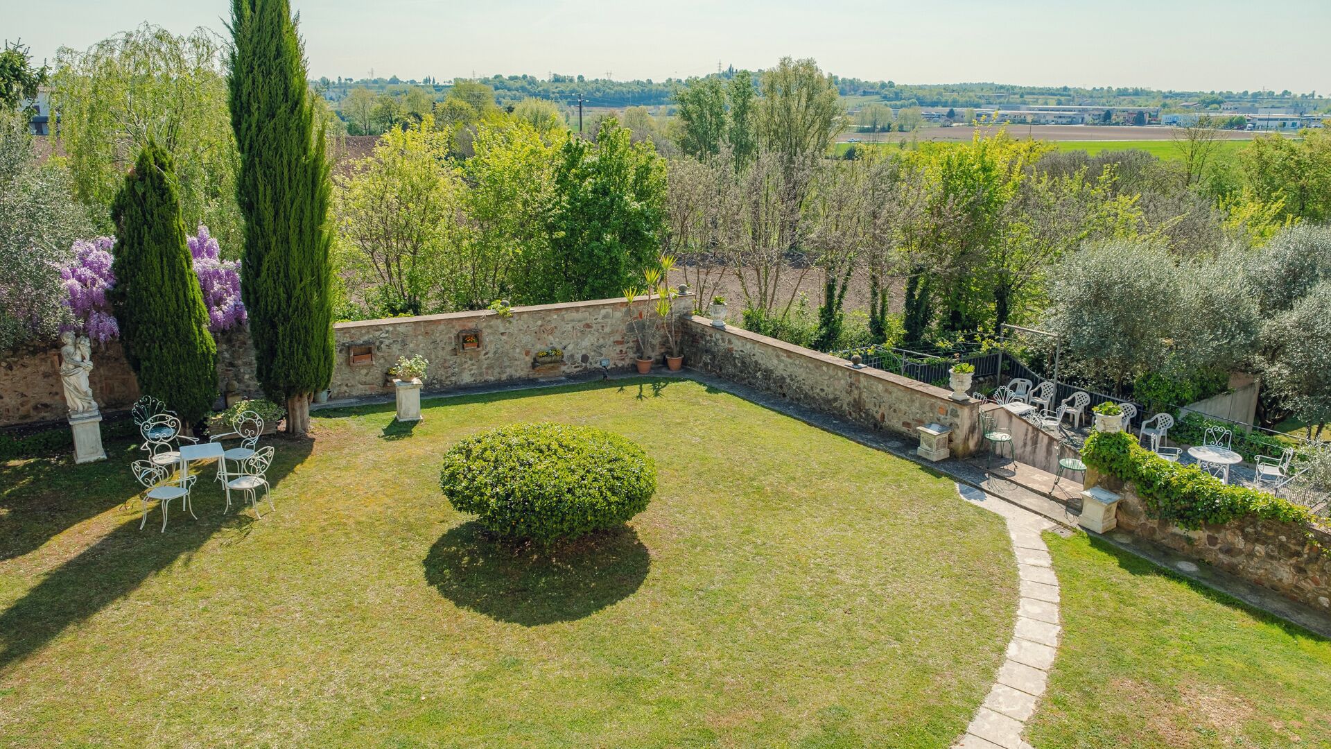 A garden with a stone wall, a small bush, and white outdoor furniture.