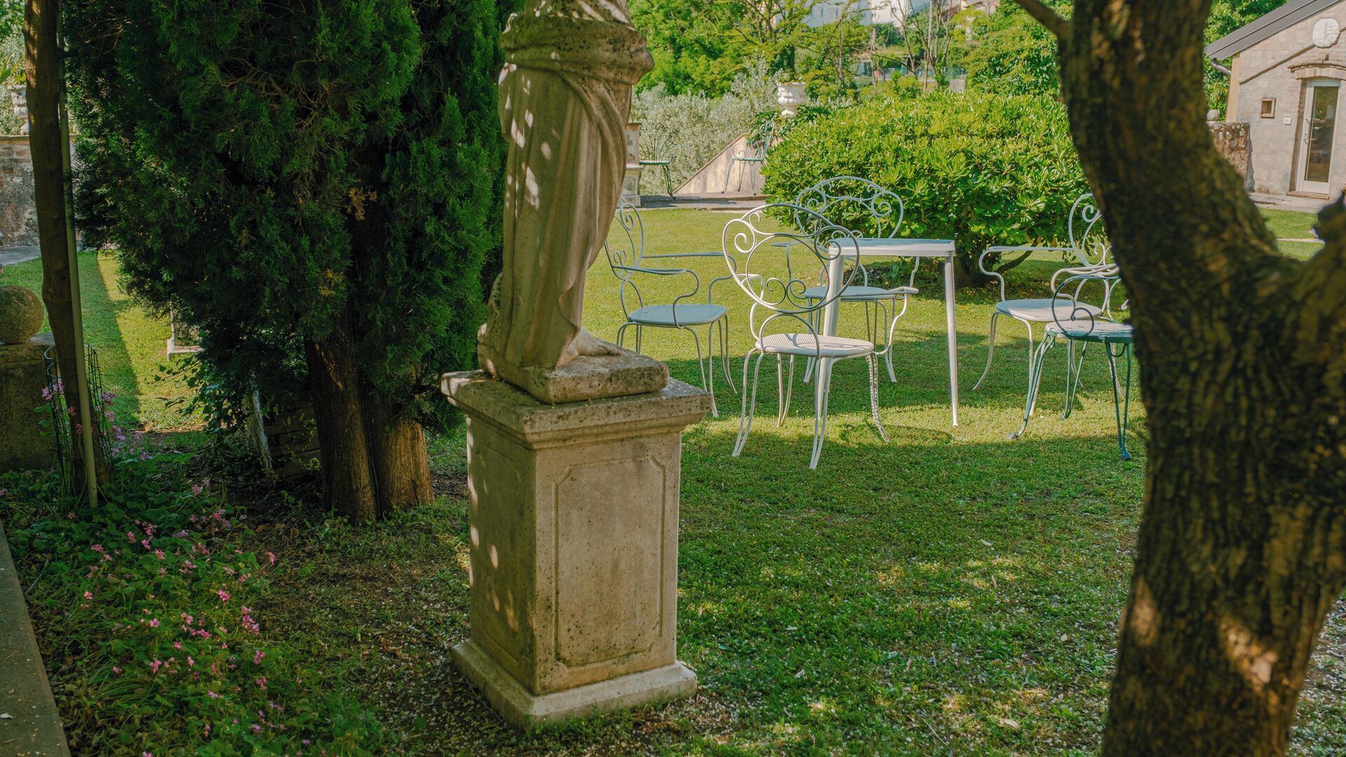 A stone pedestal with a statue, surrounded by metal chairs and a grassy area.