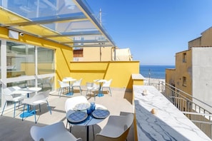 A rooftop terrace with outdoor seating, a glass enclosure, and a view of the sea. - B&B La Dimora Di Poseidone (Aspra)
