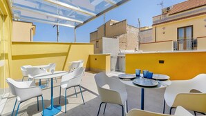 Una terraza en la azotea con mobiliario exterior, techo de cristal y vistas de edificios circundantes.