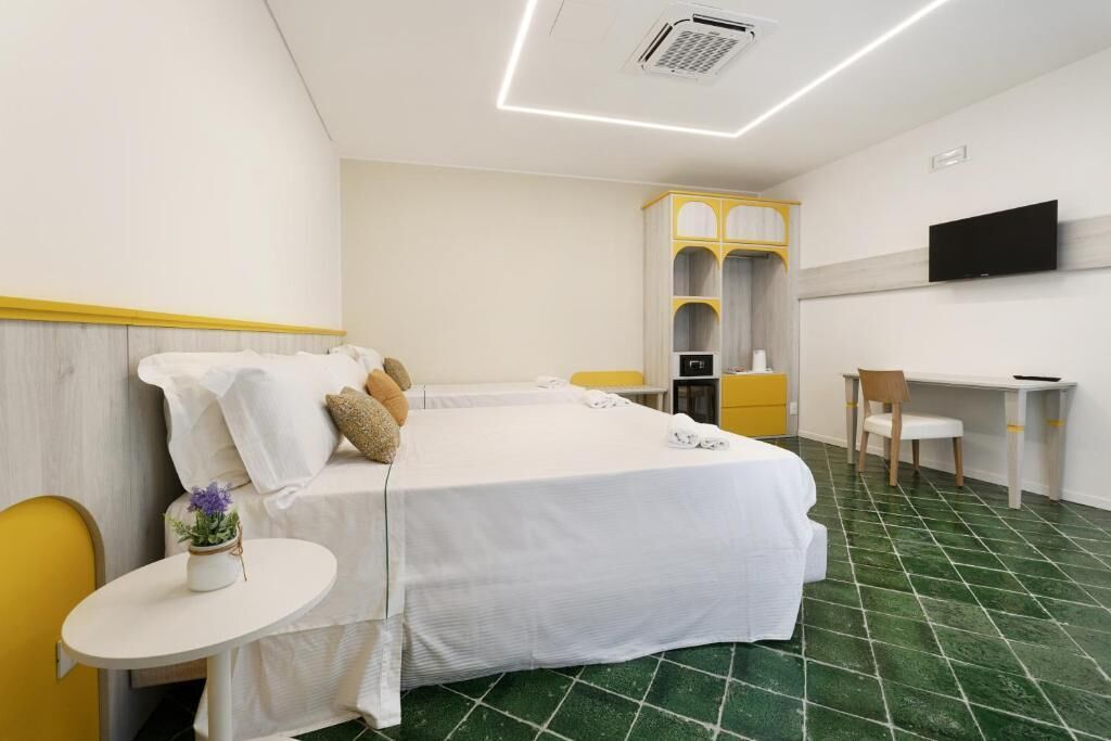 Hotelkamer met een bed, een bureau, een stoel, een televisie en een kleintje tafeltje met een plant.