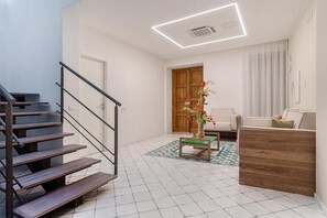 Una escalera conduce a una habitación con un escritorio de madera, una silla y un florero con flores.